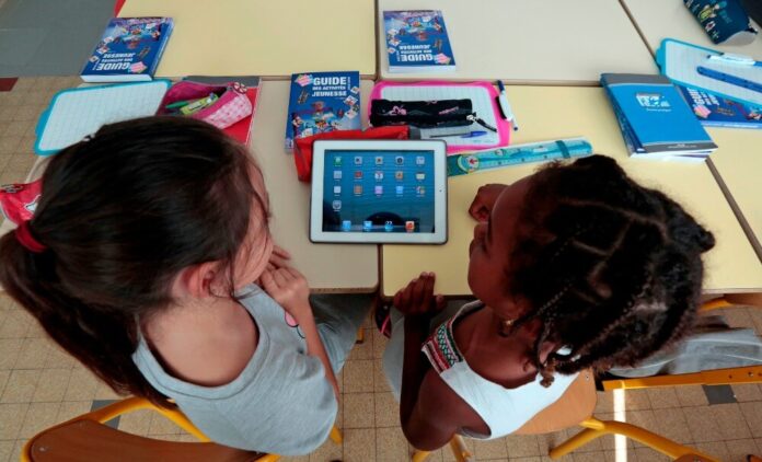Elementary school children share an electronic tablet on the first day of class in the new school year in Nice
