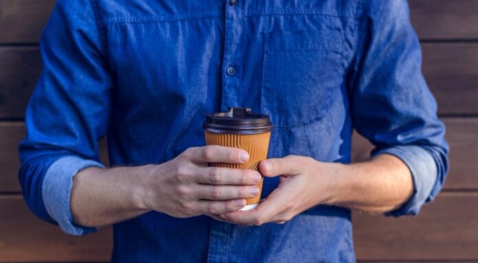Man in jeans shirt holding cup of fresh coffee against brown background
