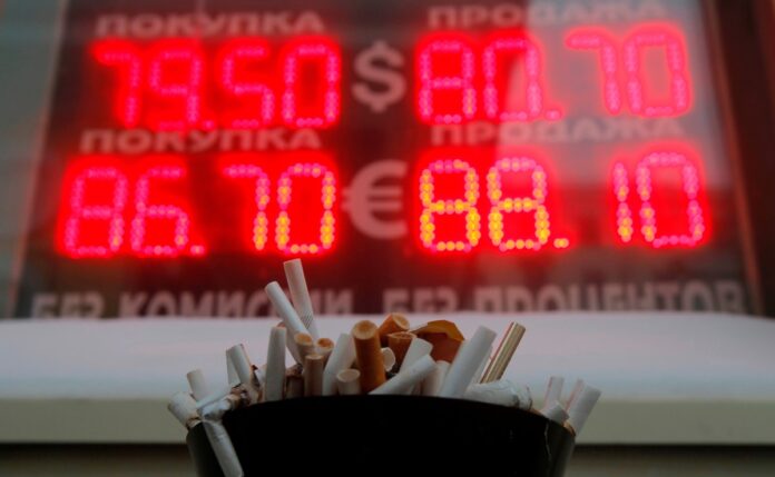 An ashtray filled with cigarette butts is seen in front of a board showing currency exchange rates of the US dollar and euro against rouble in Moscow