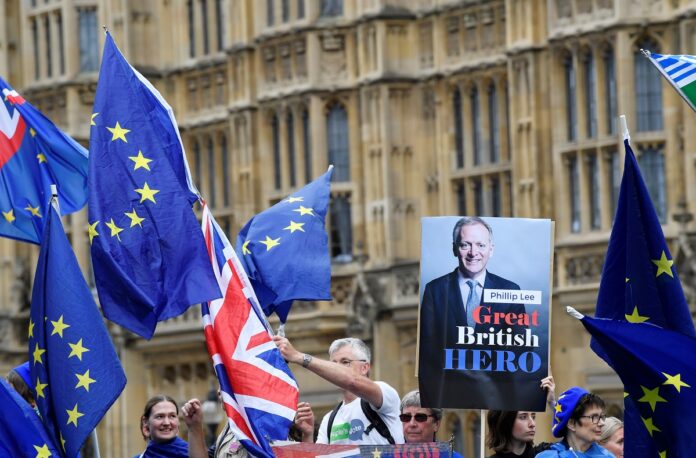Anti-Brexit demonstrators wave Union and EU flags and hold up a placard mentioning Phillip Lee, a minister who resigned today after disagreeing with the government's handling of Brexit. REUTERS/Toby Melville